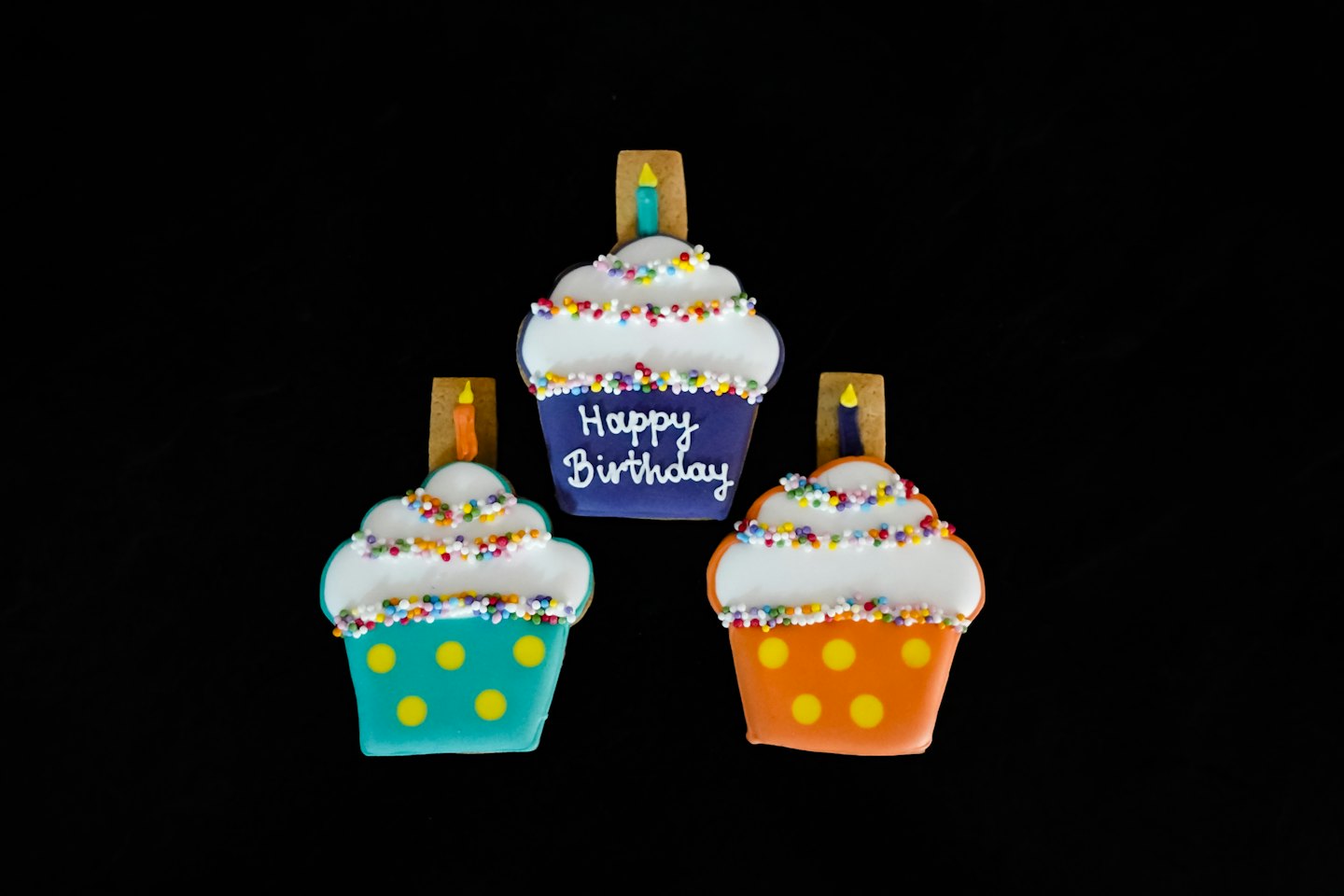 Three birthday cupcake cookies with colorful frosting on black.
