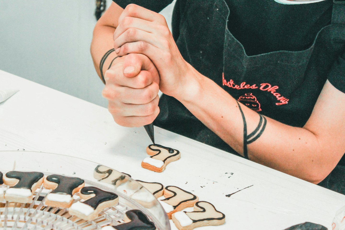 Baker pipes black icing onto small custom cookies.