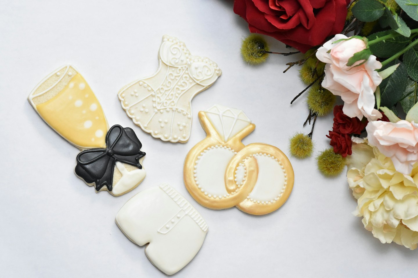 Five wedding themed sugar cookies arranged with artificial flowers.